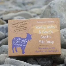 Honey, oats and goats milk soap brown cardboard box packaging with purple goat logo set on a grey pebble background