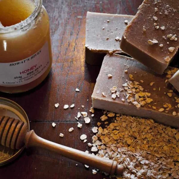 Oats and honey with a honey dipper next to a stack of honey oats and goats milk soap bars