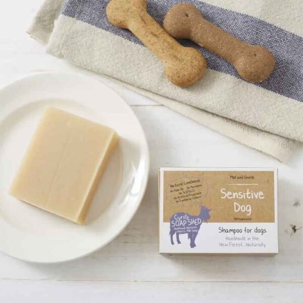 sensitive dog shampoo bar on a white plate with a card box and dog biscuits on a towel.