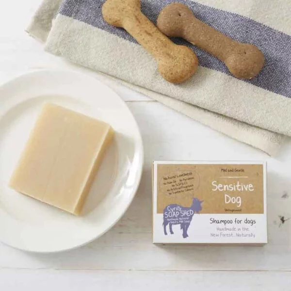 sensitive dog shampoo bar on a white plate with a card box and dog biscuits on a towel.