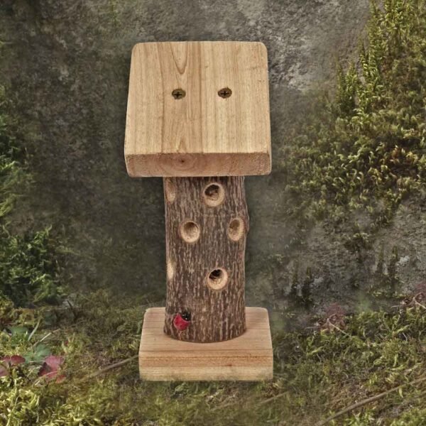 Mini Ladybird Tower in situ placed on the floor next to a tree trunk with moss growing on the trunk