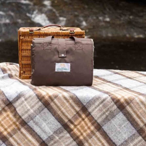 McKellar tartan Eventer Rug for picnics by Tweedmill in front of a wicker picnic hamper folded to show waterproof backing sitting on one opened out to show the tartan colours for McKellar