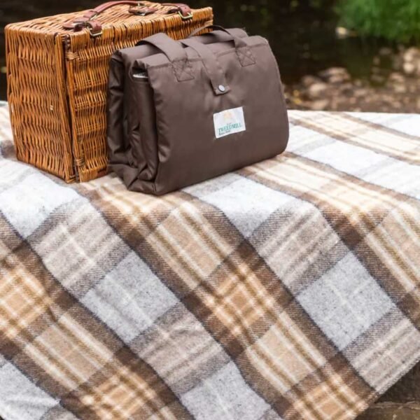 McKellar tartan Eventer Rug for picnics by Tweedmill in front of a wicker picnic hamper folded to show waterproof backing sitting on one opened out to show the tartan colours for McKellar