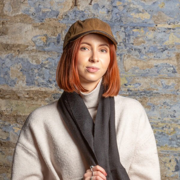 Woman with beautiful red hair facing the camera wearing a Tweedmill sand coloured wax baseball cap with dark brown leather brim