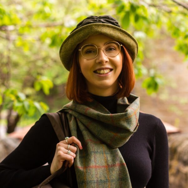 Woman with beautiful red hair facing the camera wearing a Tweedmill green wax cloche with olive green tweed brim