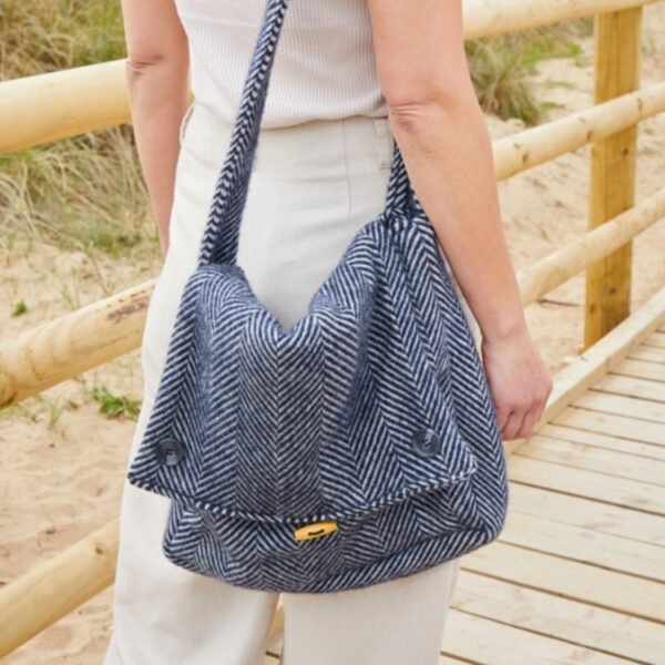 navy wool bag worn over the shoulder by a woman in beige walking near a wood post and rail fence