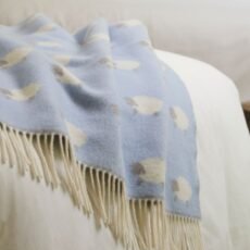 Merino wool baby blanket in blue with white sheep which have grey faces and legs laid on a light bedspread