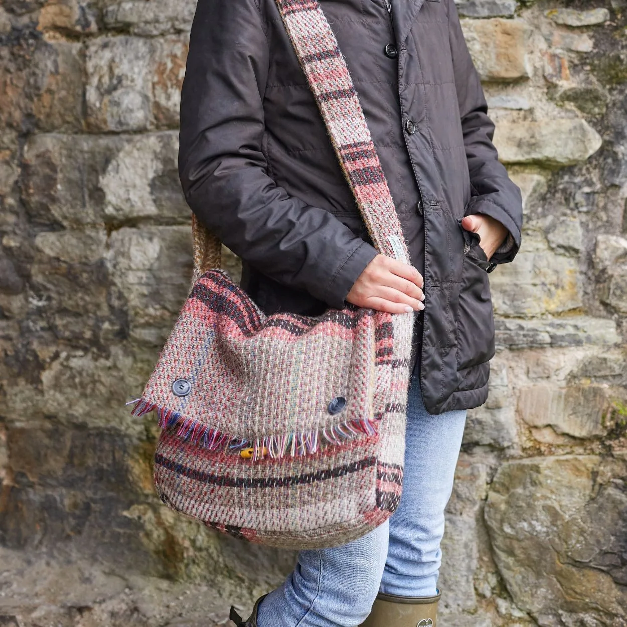 random recycled wool bag worn over the shoulder by a woman in jeans and dark coat against a stone wall