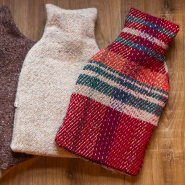 recycled wool hot water bottle x 3 on a wood table with one in dark brown, one in beige and the main one in a red, blue and beige plaid