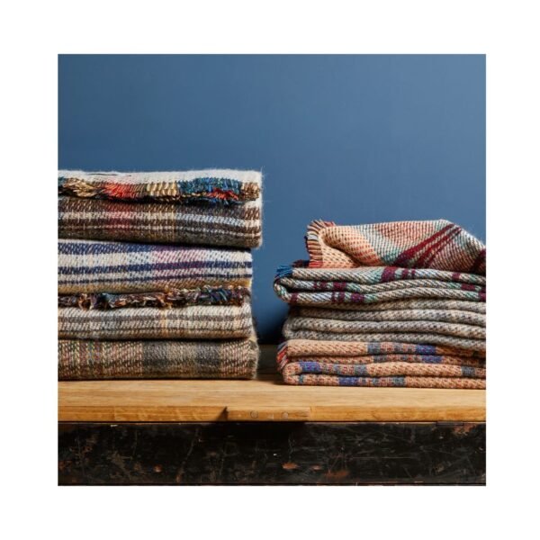 Recycled Wool Rug by Tweedmill with random colours in 2 piles on a wood table against a dark blue painted wall