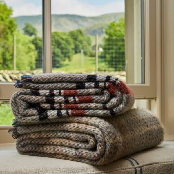 Recycled Wool Rug by Tweedmill with random colours in a pile of two by a window looking onto a country view