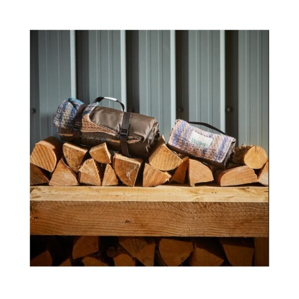 Tweedmill recycled picnic rug roll next to the smaller walker companion recycled rug roll on a pile of chopped logs in a shed