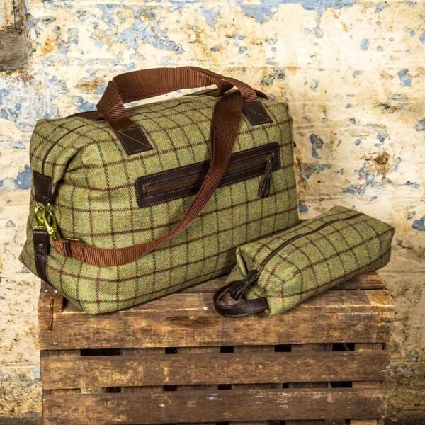 Tweed Weekender Bag with smaller wash bag in green check against a brick wall on a wood crate