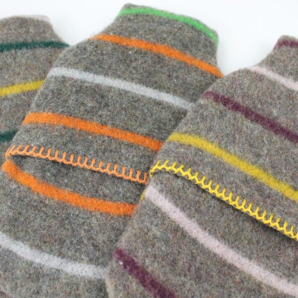 Close up of Tweedmill middle opening recycled wool hot water bottle and cover x 3 with grey background and colourful random stripes and blanket stitch