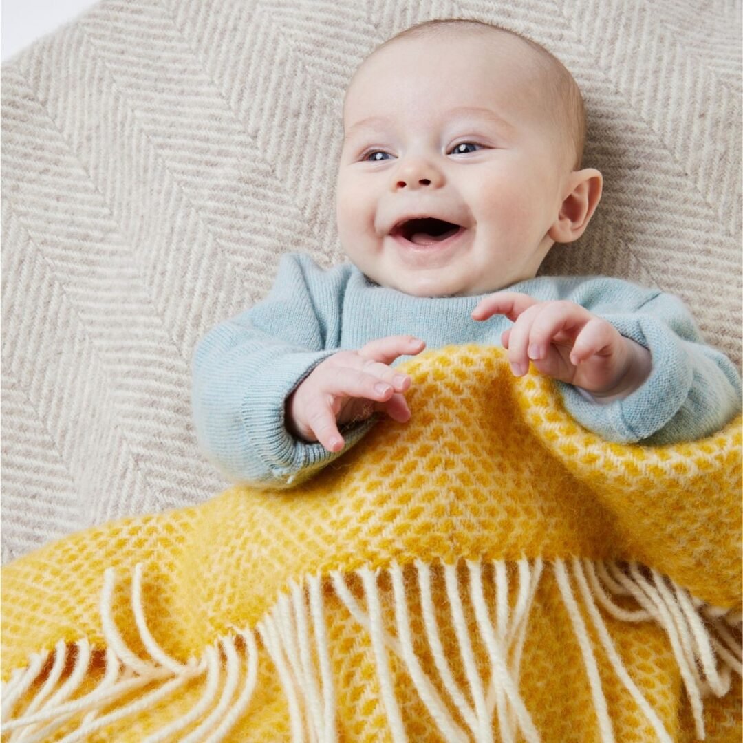 Tweedmill Beehive yellow pram blanket covering a laughing baby in a blue top