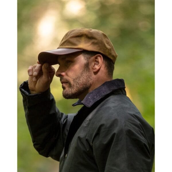 Male model facing right wearing the beige Brunswick Waxed Baseball Cap with leather brim in the outdoors