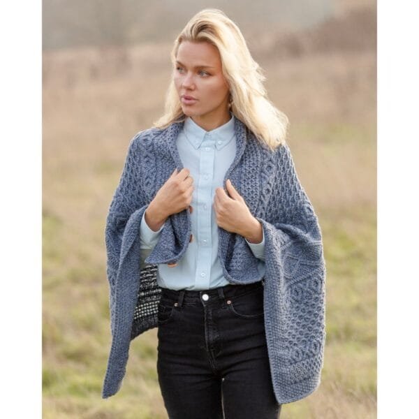 Female model wearing the sky blue 100% merino wool Remingtom Poncho in an Aran knit outside