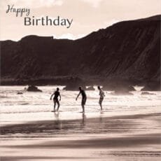 eco friendly happy birthday greeting card with 3 young men on a beach undr a cliff skimming stones in a pinkish sepia style photograph